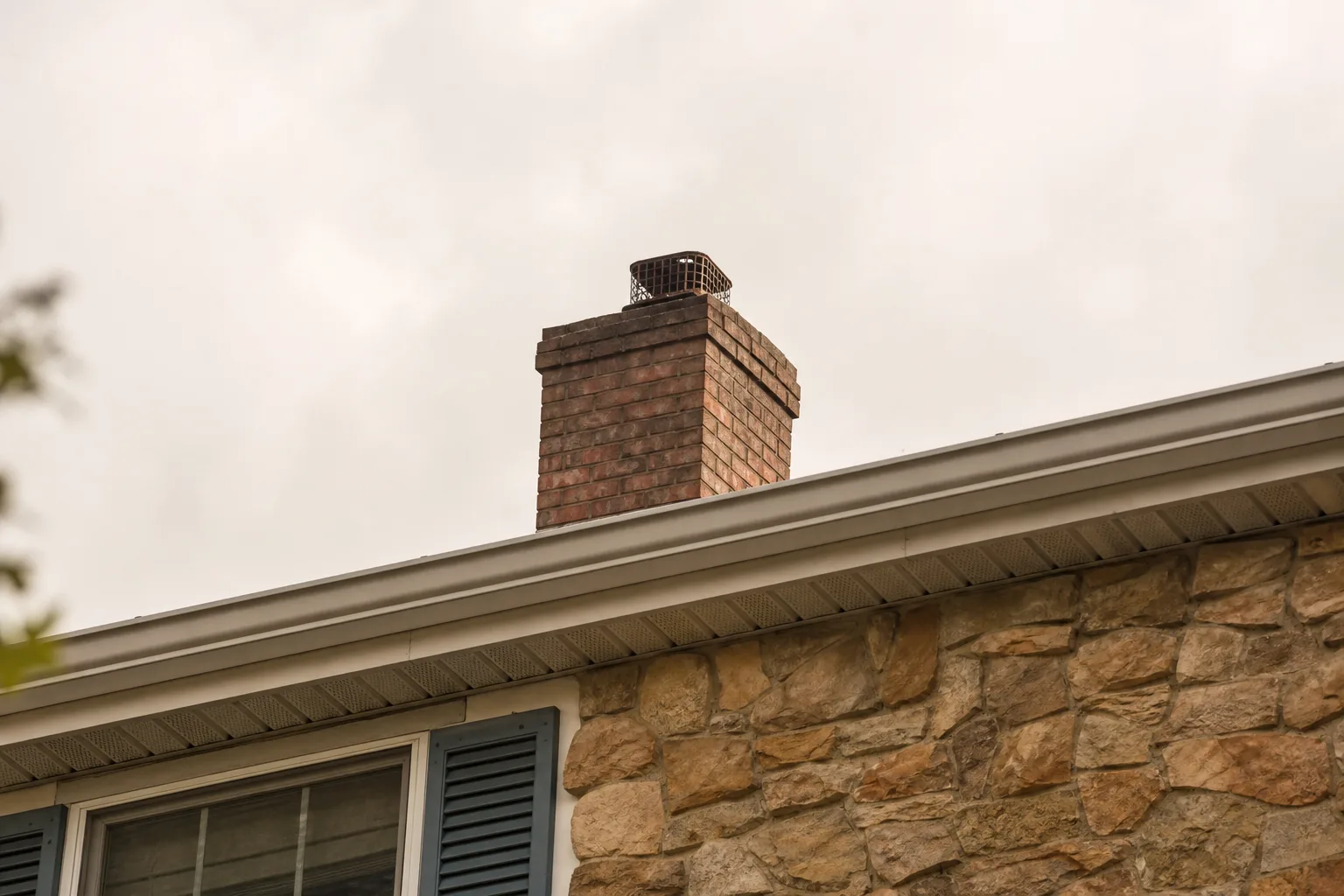 Chimney spark arrestor and cap seen from the driveway looking up at a house roofline