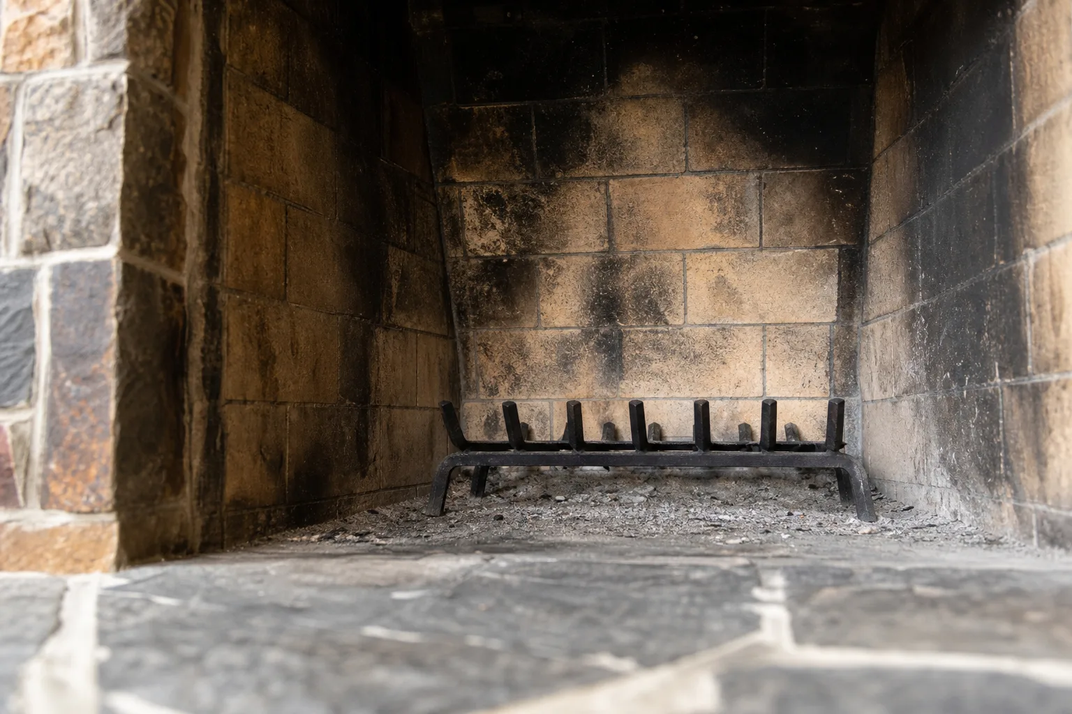 The fireplace firebox from hearth level, showing sooty firebrick, the sloping back wall and an empty grate