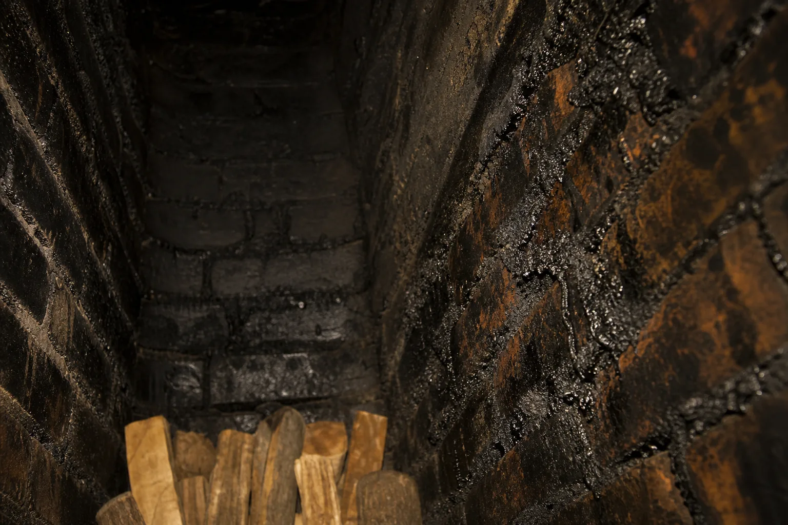 Thick black creosote glaze coating brick flue walls above a fireplace smoke chamber