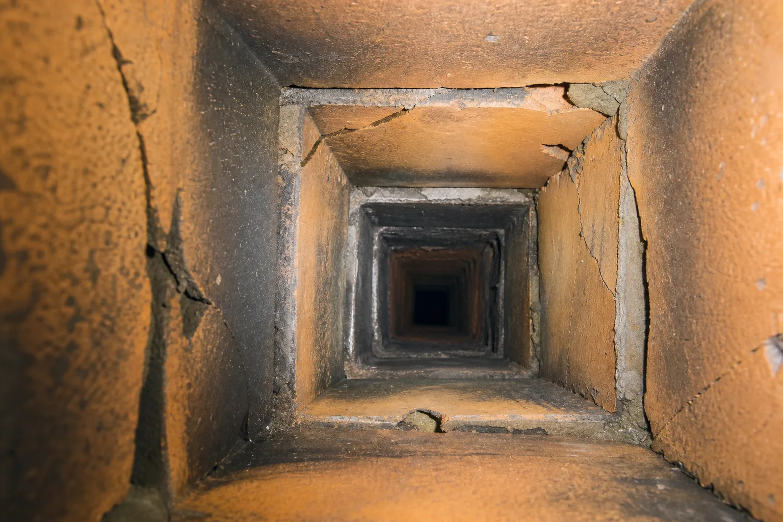 Chimney liner installation before condition: interior view of a deteriorated clay tile flue with cracked tiles and open mortar joints
