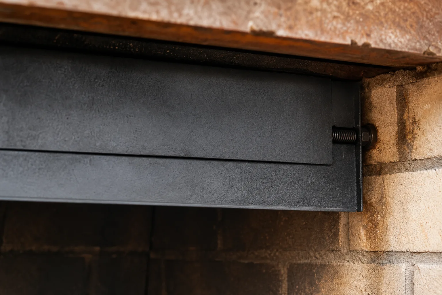 Fireplace smoke guard close up showing the telescoping overlap seam and spring end against the firebrick wall