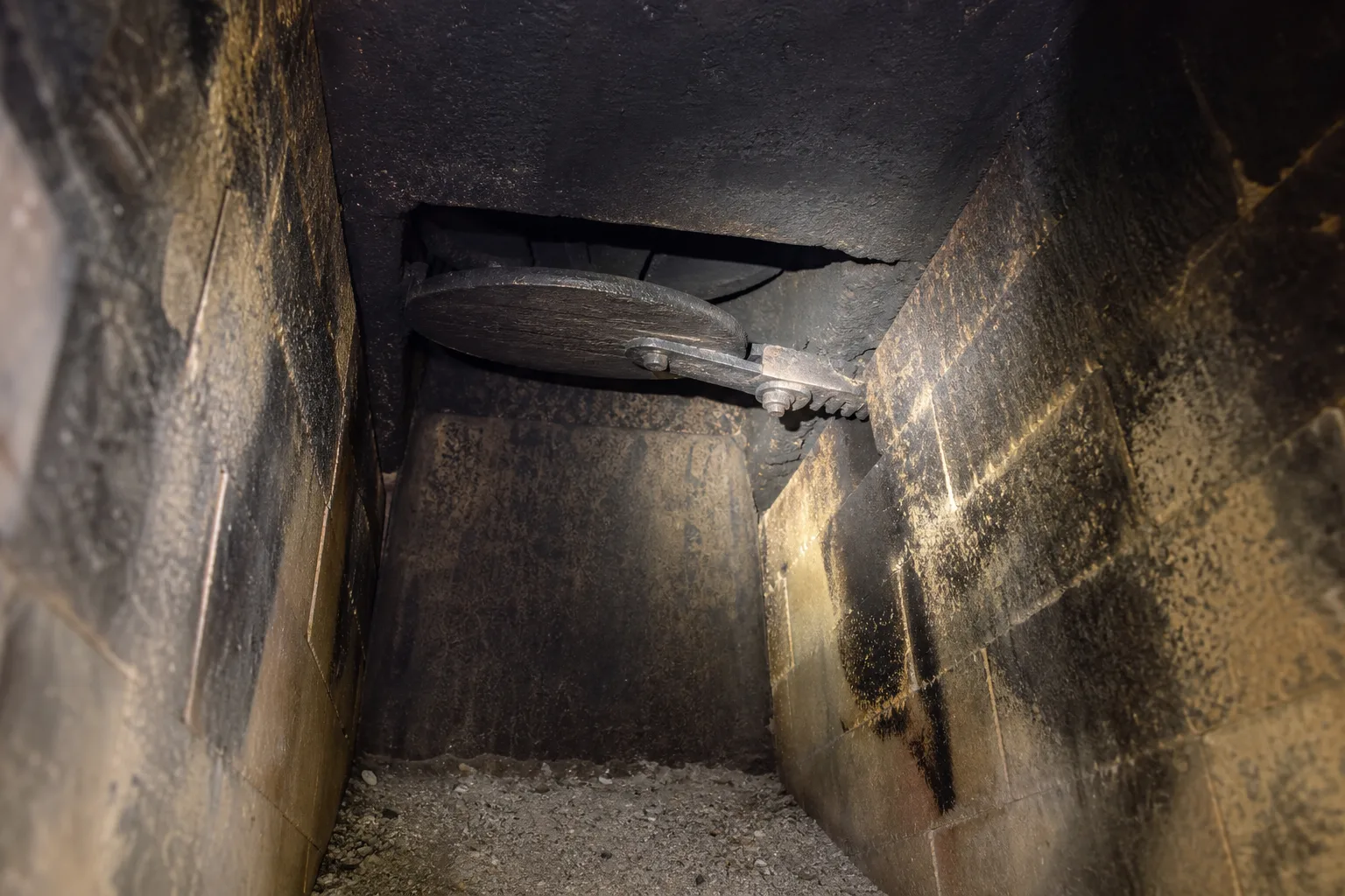 Fireplace smoke guard diagnosis: flashlight on an open cast iron damper plate inside a sooty masonry firebox