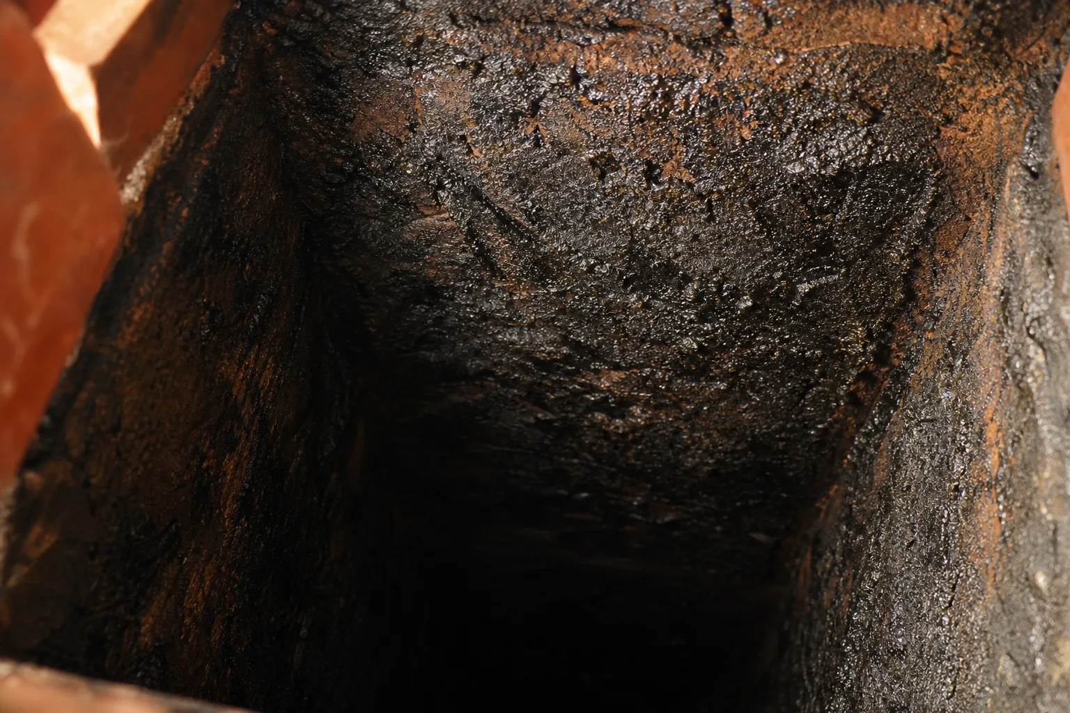 How to clean a chimney: a flue wall in typical worn condition with heavy glazed creosote buildup