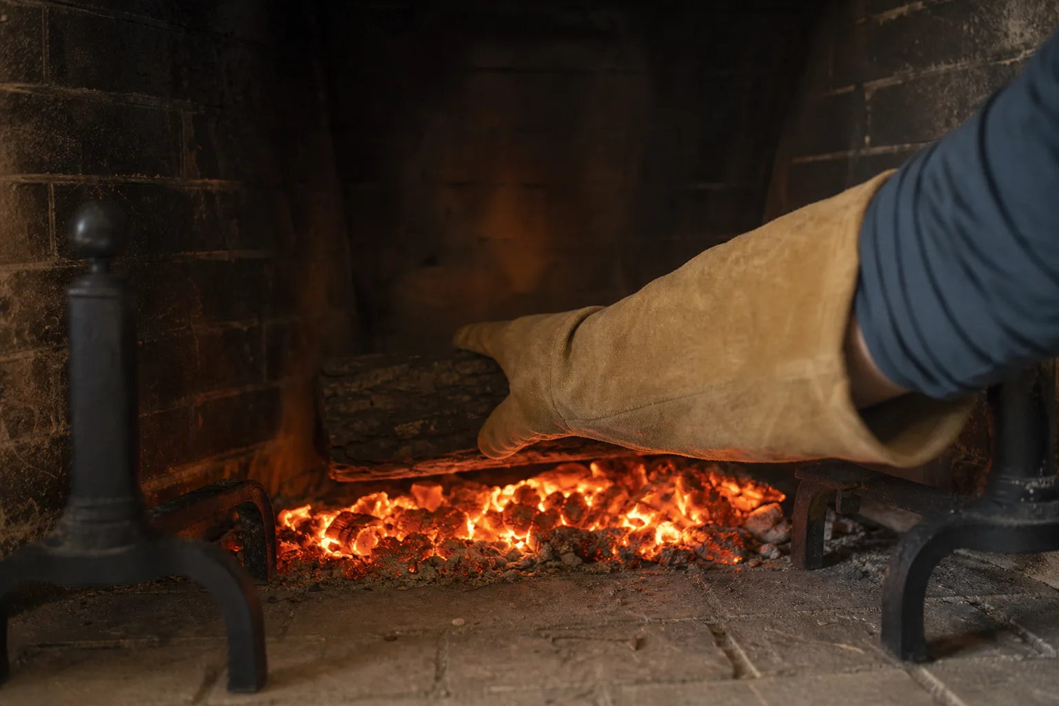 Fireplace gloves with a long gauntlet cuff protecting a forearm reaching over glowing embers