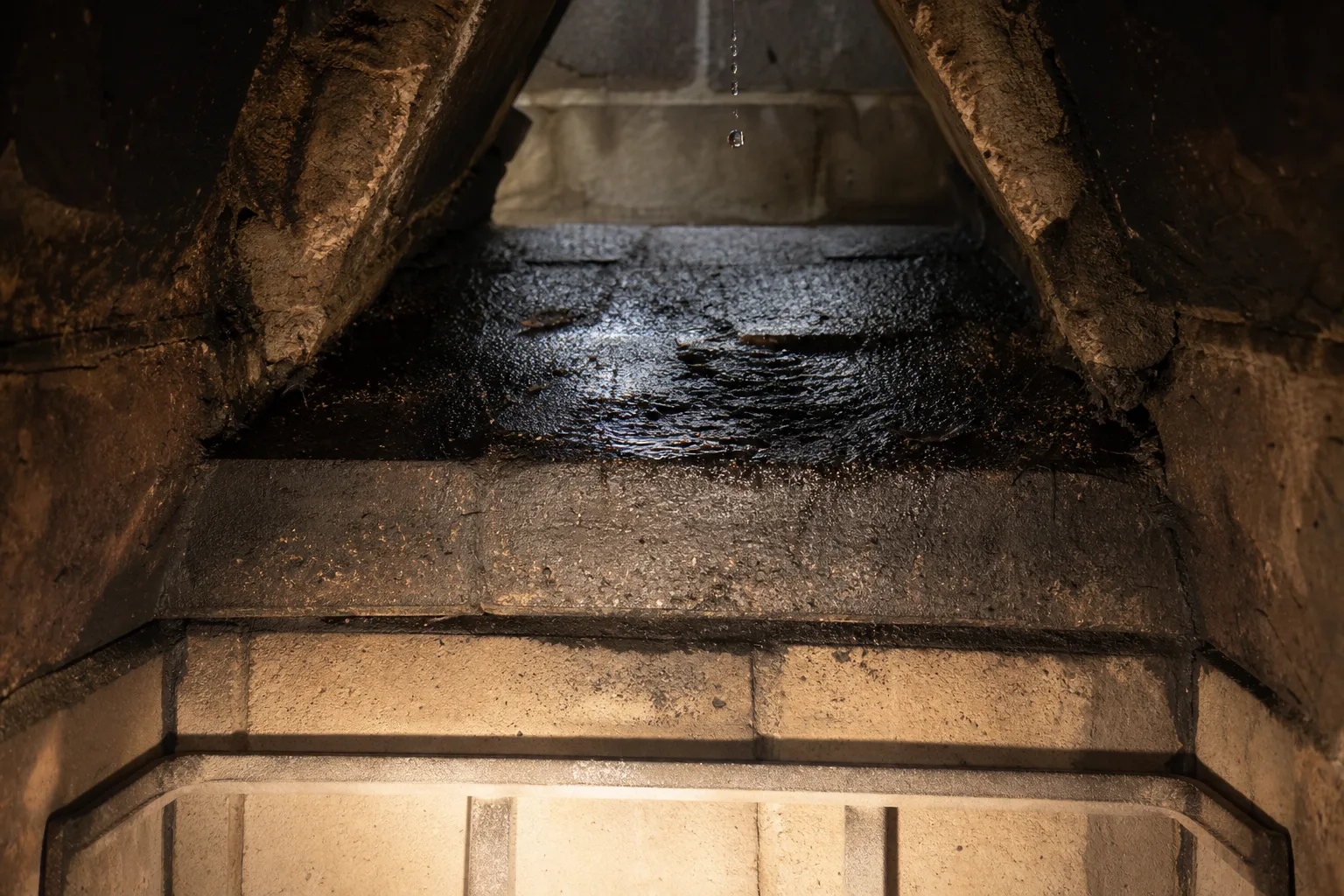 Rainwater pooled in wet black soot on a fireplace smoke shelf behind the damper