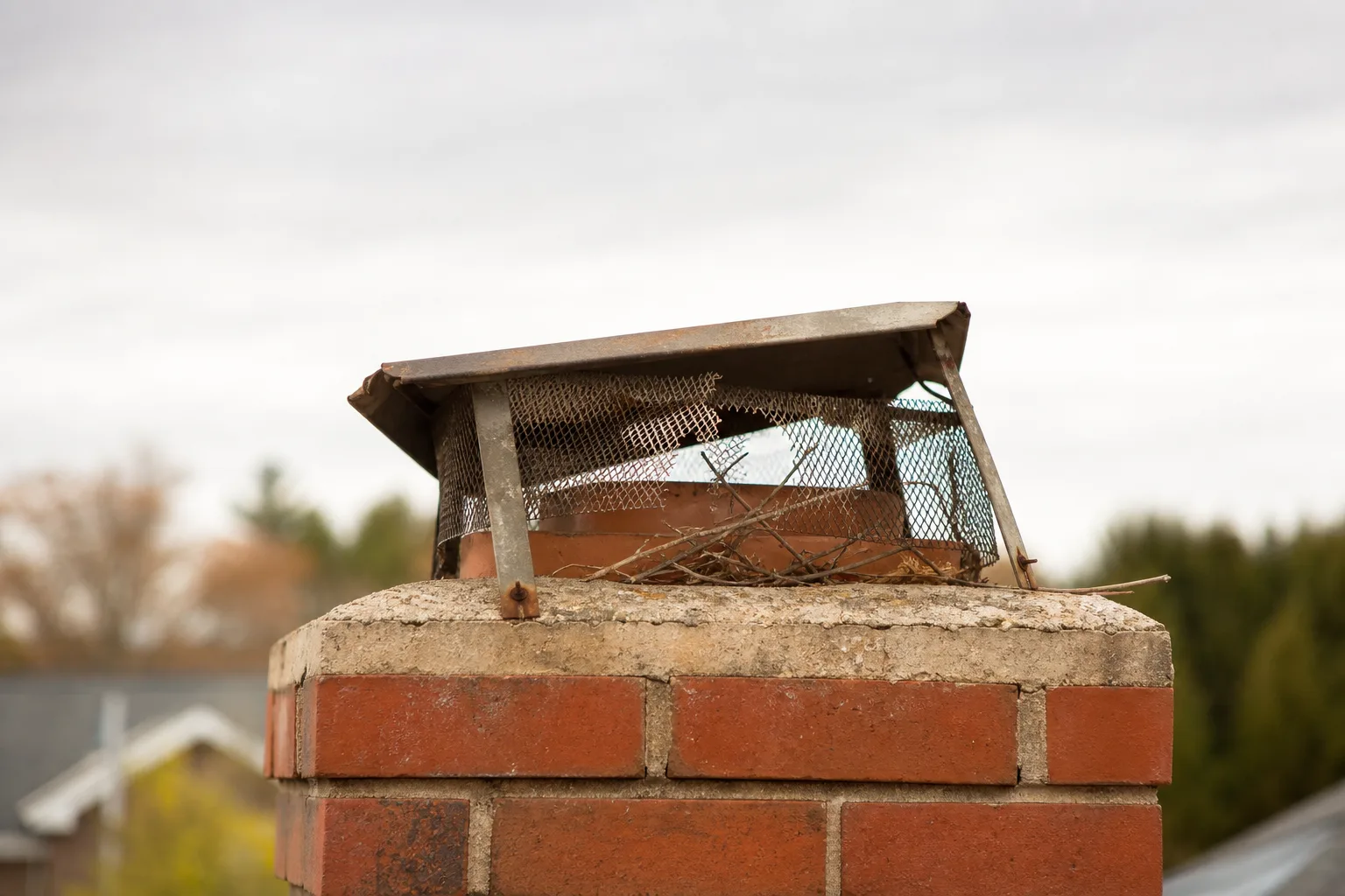 Tilted chimney cap with torn mesh and rust on a brick chimney