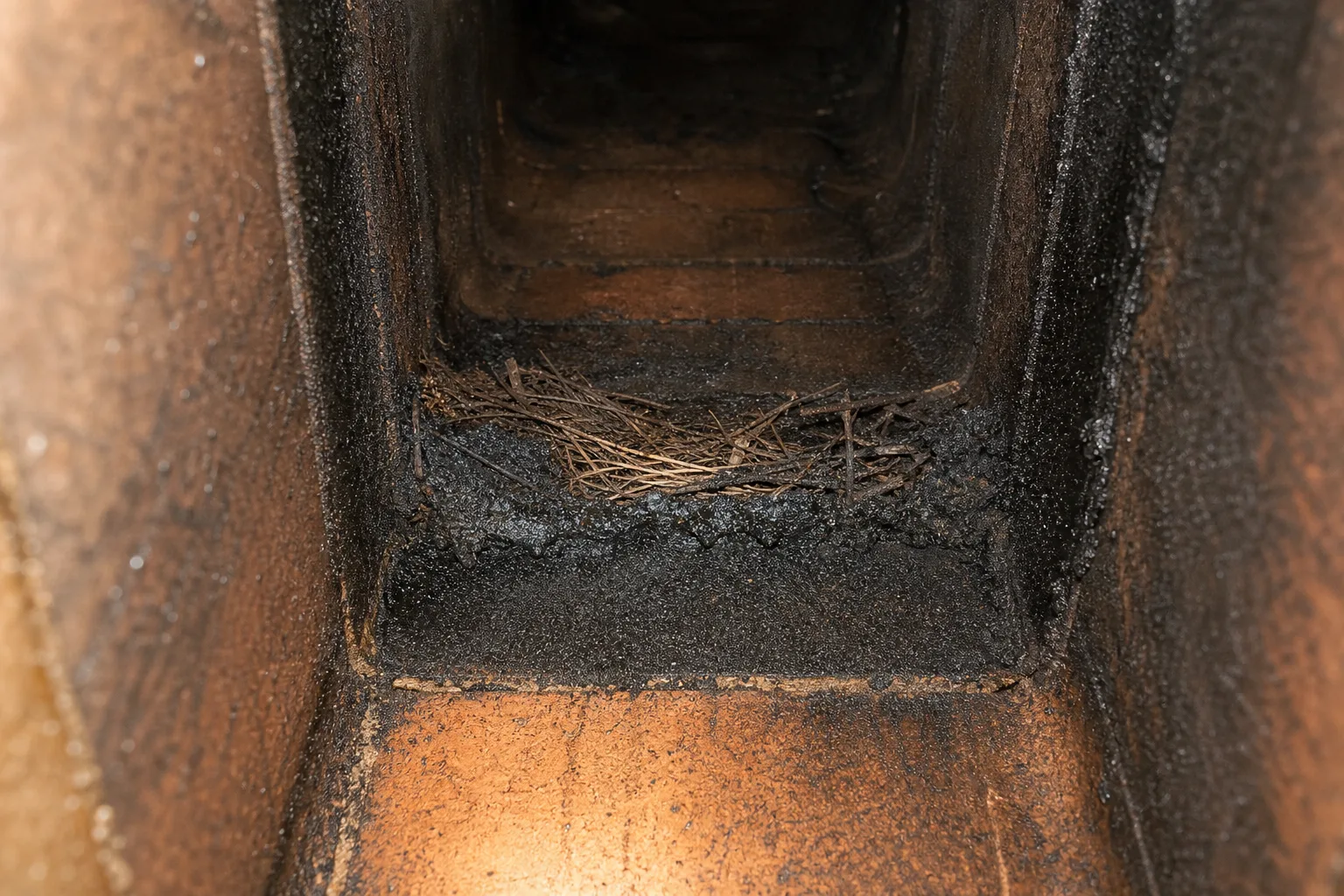 Heavy flaky creosote and twig debris inside a clay tile flue seen from below