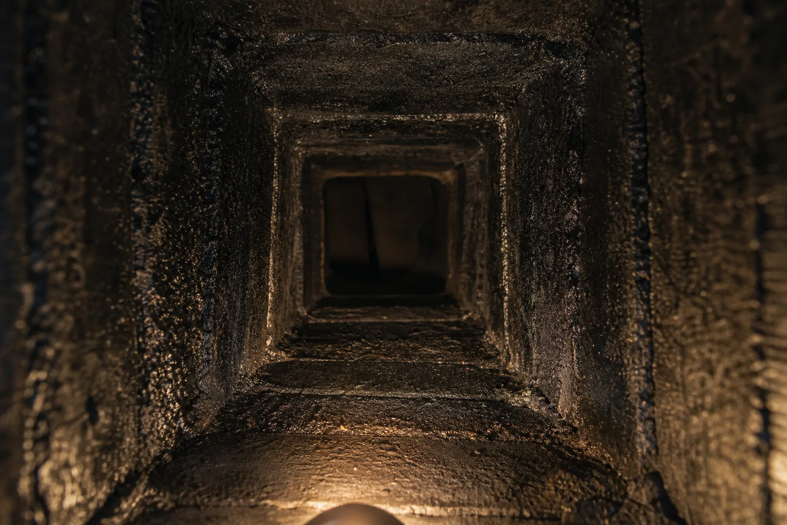 Looking up a flue where clay tiles are coated in thick glazed black creosote