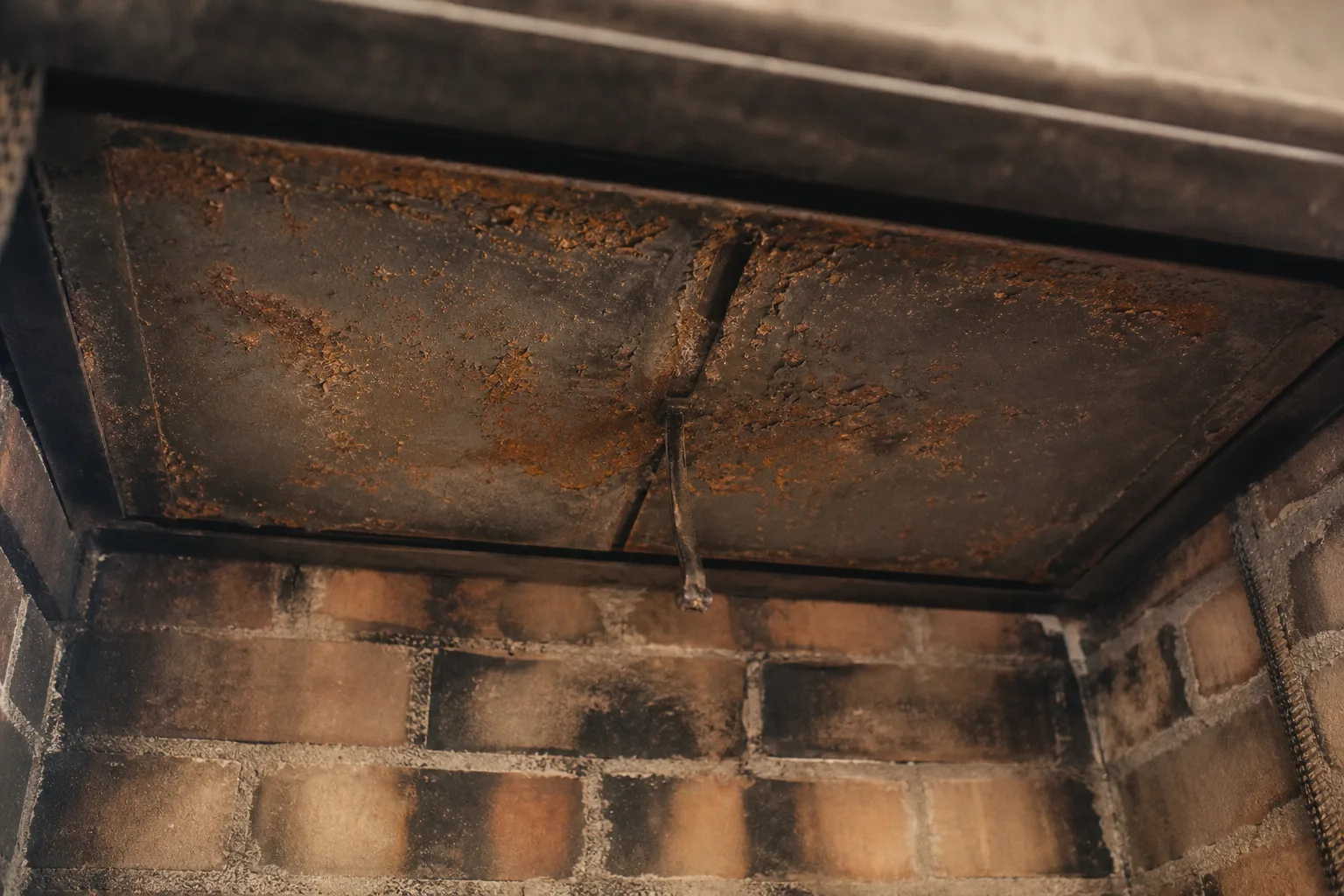 Looking up inside a firebox at a damper plate with rust stains and flaking metal