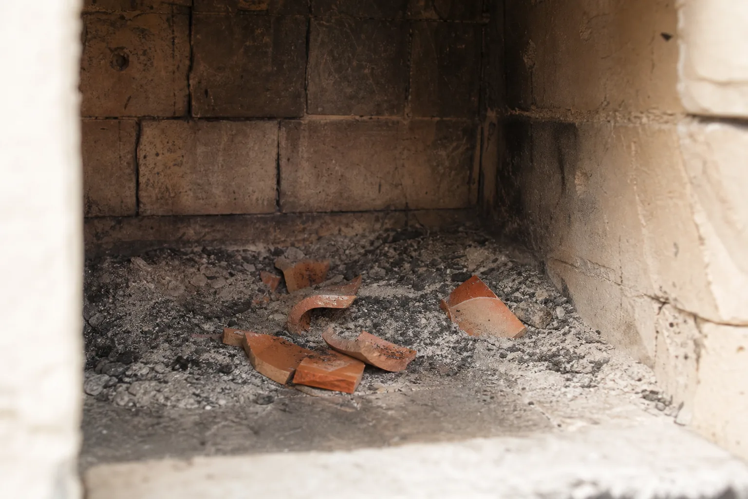 Broken orange clay flue tile fragments scattered in a fireplace firebox among ash